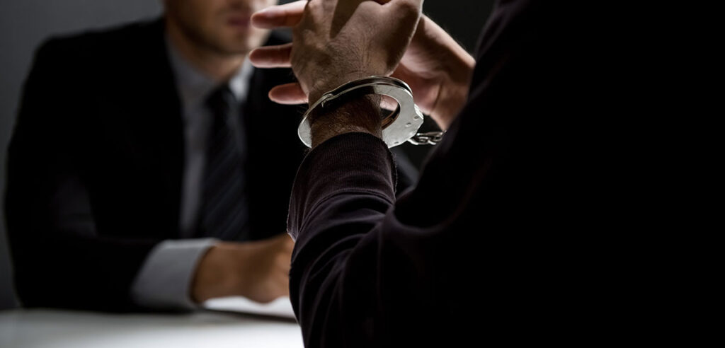 Man at a desk in handcuffs - Criminal Justice and Probation Services